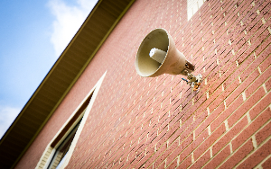 An intercom is attached to an outside brick wall where announcements are given for students